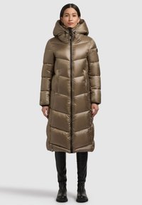 Lang, hætteklædt dynejakke i en varm beige farve med quiltede paneler, en lynlås foran og sidelommer. Glat, skinnende tekstur.