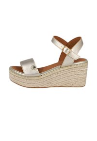 Sandalia plataforma metálica dorada con dos correas anchas, una correa ajustable en el tobillo y un tacón cuña envuelto en yute. Textura suave.