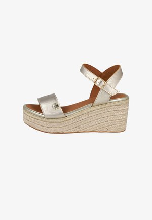 Sandalia plataforma metálica dorada con dos correas anchas, una correa ajustable en el tobillo y un tacón cuña envuelto en yute. Textura suave.