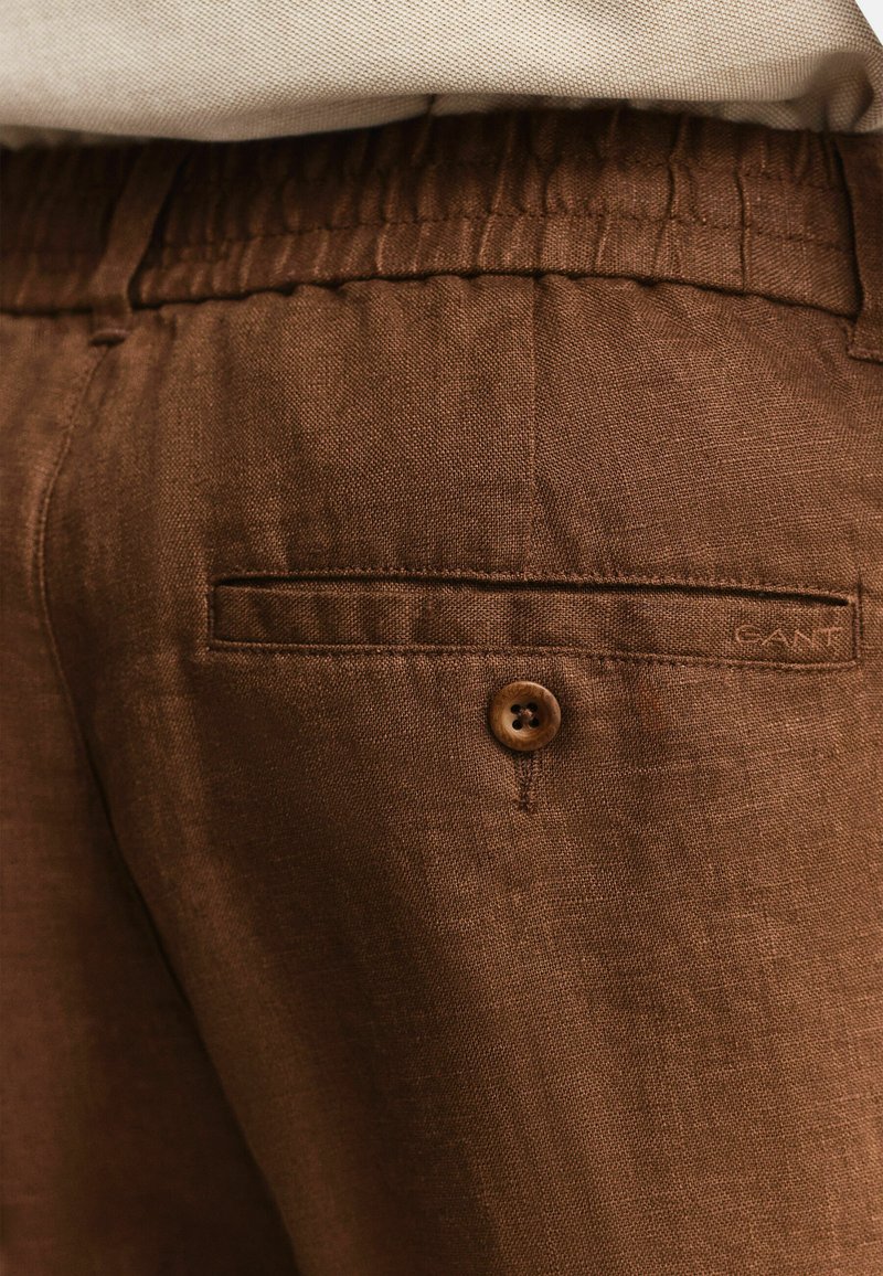 Nahaufnahme von braunen Leinenhosen mit elastischem Bund, einer Gesäßtasche und Knopfdetail.