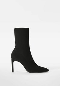 Czarny botek na kostkę wykonany z elastycznej tkaniny, z charakterystycznym spiczastym noskiem i wysokim szpilkowym obcasem. Gładka, gładka faktura z minimalną ilością szwów.