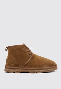 Botines de ante marrón con un acabado texturizado, que cuentan con dos ojales, punta redondeada y una suela de goma flexible con surcos pronunciados.