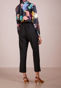 Blouse en satin noir à motifs floraux vifs, associée à un pantalon noir fuselé et des sandales à talons bruns. Vue arrière montrant une taille élastique.