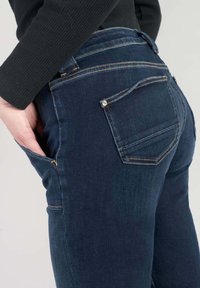 Mörkblå denimjeans med en åtsittande design, som har två bakfickor med synlig sömnad och detaljer i guld.