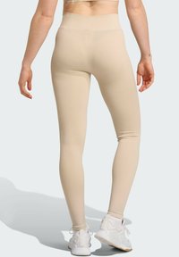 Beige high-waisted legging met een gestructureerd ribbelpatroon, gladde stof en enkel lengte, gecombineerd met witte sportschoenen.