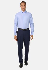 Světle modrá košile s dlouhým rukávem a límcem na knoflíky, v kombinaci s tmavě modrými formálními kalhotami a černými botami. Materiál vypadá hladce s jemným vzorem.