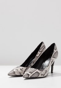 Spidsede højhælede sko med sort og hvidt slangeprint, lavet af tekstureret materiale, med en slank hæl.