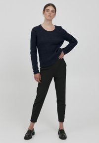 Marinblauer gestrickter Pullover mit rundem Halsausschnitt und strukturiertem Muster, kombiniert mit schmalen schwarzen Hosen und schwarzen Slippern.