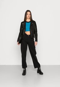 Veste en cuir noir sur un haut court rayé bleu et noir, associée à un pantalon large noir et des bottines avec quincaillerie décorative.