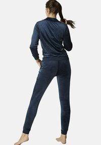 Ensemble de loisirs en velours bleu marine comprenant un haut à manches longues avec un col et un pantalon ajusté à poignets, texture lisse et design ajusté.