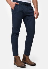 Granatowe, dopasowane spodnie z miękkiego materiału z zamkiem błyskawicznym, szlufkami na pasek i bocznymi kieszeniami, zestawione z brązowymi botkami za kostkę.