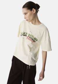 T-shirt oversize color crema in cotone con stampa grafica audace in verde e rosso. Maniche corte e scollatura rotonda.