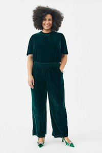Groen fluwelen twee-delige outfit bestaande uit een top met korte mouwen en broeken met elastische tailleband. Aangevuld met puntige groene schoenen met versieringen.