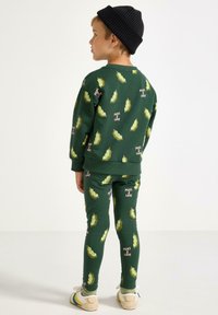 Grøn sweatshirt og leggings sæt med et "Ærter og kærlighed" mønster. Blødt materiale, tætsiddende design og ribbede manchetter. Afsluttet med en sort beanie.