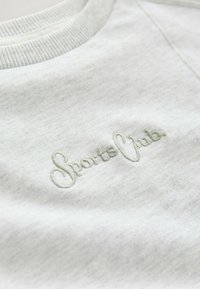 Light gray sweatshirt with ribbed neckline; features embroidered "Sports Club" logo in a slightly darker shade. Soft texture.
