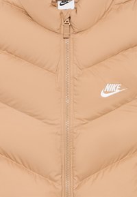 Bežna podložena bunda s chevron vzorcem. Ima sprednji zadrgo in vezeno Nike logo v beli barvi. Gladka tekstura in visok ovratnik.
