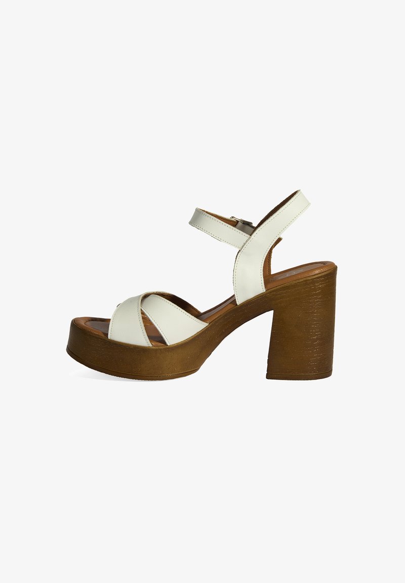 Sandales en cuir blanc à plateforme avec un talon épais et texturé brun, avec des lanières croisées et une sangle de cheville réglable.