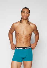 Teal boxer briefs made of stretch fabric featuring a black waistband with white branding. Smooth texture and fitted design.