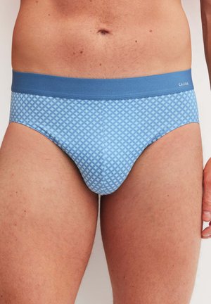 Man draagt lichtblauwe slip met patroon en een effen blauwe tailleband, staand tegen een neutrale achtergrond.