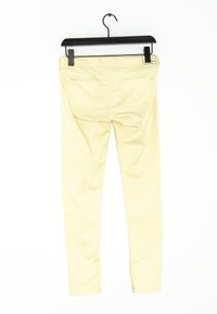 Jeans skinny de mezclilla amarillos con una textura suave, bolsillos traseros que presentan un patrón de costura ondulada, y una cintura tradicional con trabillas para cinturón.