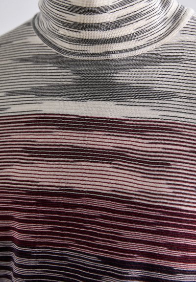 Megztinis su aukštu kaklu, puoštais horizontaliomis juostelėmis juodos, pilkos ir sodriai raudonos spalvos, su įvairių pločių juostomis ir minkšta, tekstūruota apdaila.