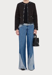 Veste bomber noire matelassée avec fermetures à boutons-pression métalliques, associée à un jean en denim bleu à jambes larges avec des panneaux bleu clair contrastants et un sac à main noir.