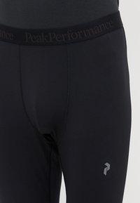 Black athletic leggings with a wide elastic waistband featuring "PeakPerformance" branding. Smooth texture with a fitted design and logo detail.