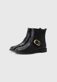 Botas de tornozelo em couro preto com bico arredondado, sola plana e uma correia com detalhe em fivela dourada. Textura suave, design de altura média.