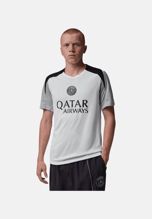 En mand iført en hvid og sort Paris Saint-Germain sportsjersey med Qatar Airways-logo og sorte shorts med PSG-emblem.