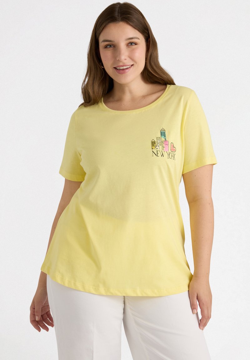 Camiseta de algodón amarilla con mangas cortas y cuello redondeado, que presenta un gráfico bordado de "New York" en detalles multicolores en el pecho.