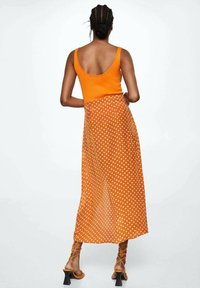 Oranje geribbelde tanktop gecombineerd met een lange, doorschijnende rok met stippen. Chique sandaaltjes met hakken maken de outfit af.
