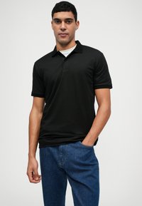 Black polo shirt with a classic collar and short sleeves, made of smooth fabric, paired with blue denim jeans, featuring a relaxed fit.