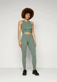 Lys grønn treningssett med en cropped topp med knutepunkt og høyt liv leggings, laget av myk, elastisk stoff. Svart sneakers.