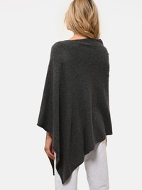 Poncho de lana gris con un ajuste holgado, dobladillo asimétrico y textura suave. Sin patrones visibles ni accesorios. Lleva puesto sobre pantalones blancos.