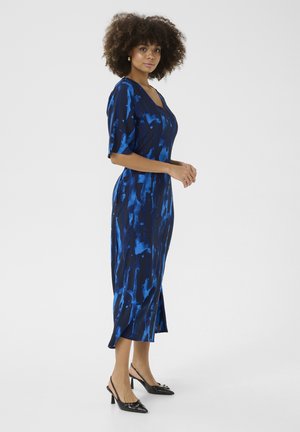Blue and navy patterned dress with short sleeves, midi length, and a straight cut. Worn with black pointed-toe heels. Smooth fabric texture.