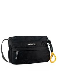 Bolsa de tela negra con un bolsillo frontal con cremallera, parche de logo de marca y un acento amarillo en forma de lazo. Cuenta con una correa desmontable para llevar.