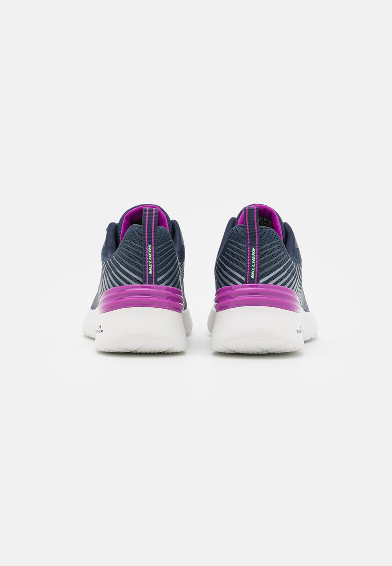Zapatillas de running con una parte superior de malla de color azul oscuro, suela blanca y prominentes acentos morados en el talón y el cuello. Patrón de rayas horizontales.