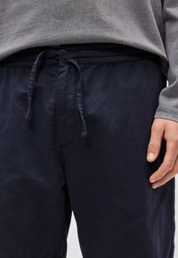 Σκούρο μπλε παντελόνι με ελαστική μέση και κορδόνι. Το ύφασμα φαίνεται λείο, με άνετη εφαρμογή και ελάχιστες ραφές.