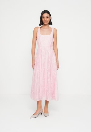 Μακρύ ροζ φόρεμα με τετράγωνη λαιμόκοψη, κεντήματα με λουλούδια και ροή φούστας. Συνδυάζεται με γκρι ψηλοτάκουνα παπούτσια με μυτερή μύτη.