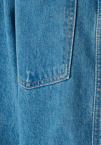 Ljusblå denimtyg med synlig textur. Har en ficka med lappar och kontrasterande orange sömmar längs kanterna.