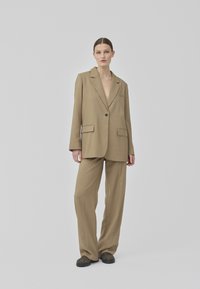 Un blazer oversized bej, cu un singur nasture, asortat cu pantaloni lejeri, cu o croială dreaptă și un design minimalist.