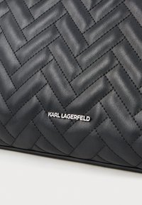 Fekete steppelt bőr felület cikkcakk mintával és ezüst "KARL LAGERFELD" logóval.