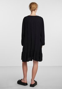 Vestido negro de manga larga con un corte holgado, con un dobladillo con volantes. Fabricado en tejido ligero, tiene un escote cuadrado y una textura suave.