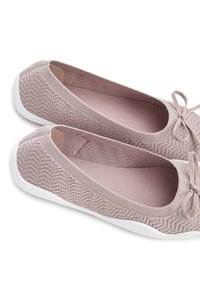 Bailarinas de punto rosa claro con una superficie texturizada y suelas de goma blanca, que cuentan con un lazo decorativo cerca de la abertura frontal.