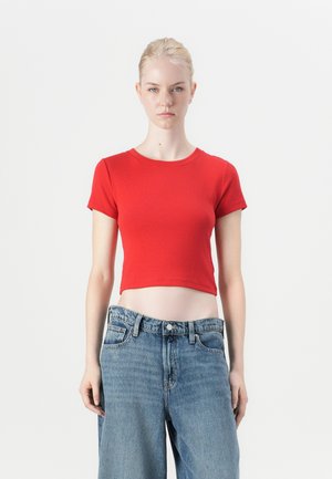 T-shirt rouge court en coton, avec des manches courtes, un col rond, et une texture lisse, associé à un jean taille haute bleu clair.