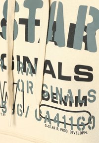 Felpa beige con cappuccio caratterizzata da un grande testo grafico in verde e nero, dotata di tasca a marsupio e coulisse. Realizzata in morbido cotone.