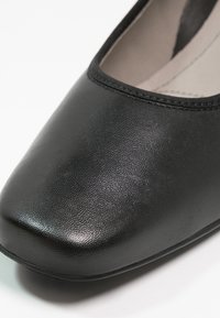 Gros plan sur une chaussure plate en cuir noir avec un bout carré arrondi et un bord cousu le long de l'ouverture.