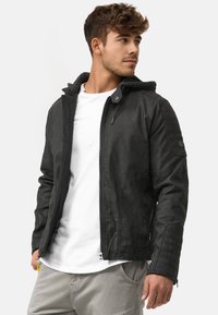 Schwarze Lederjacke mit Kapuze, mit gesteppten Akzenten an den Schultern, einem Reißverschluss und Seitentaschen. Über einem weißen T-Shirt getragen.