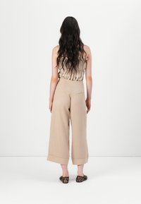 Pantalons beige à jambe large avec taille haute, en tissu texturé et avec des ourlets repliés ; associés à un haut léger et ondulé. Des ballerines à imprimé animal sont portées.