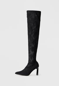 Botas negras de tacón alto por encima de la rodilla, hechas de tejido texturizado, con puntera afilada y un tacón brillante alto con un patrón parecido a encaje.